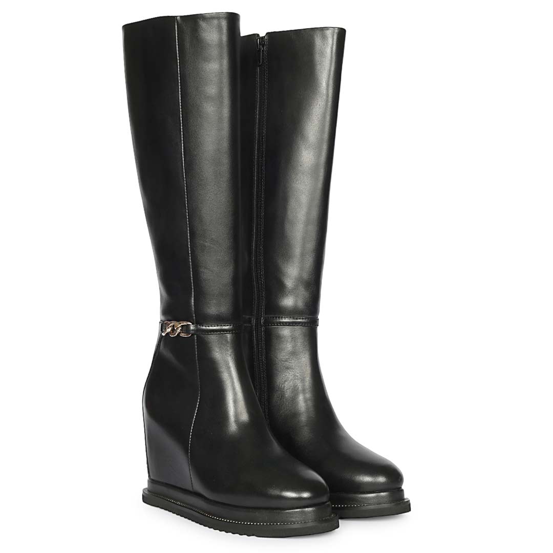 A pair of black leather knee-high wedge boots with a small gold-tone chain detail on the side