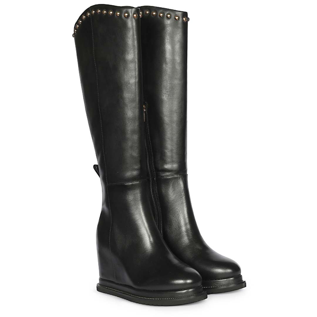 A pair of black leather knee-high boots with a wedge heel and decorative metal studs along the top collar