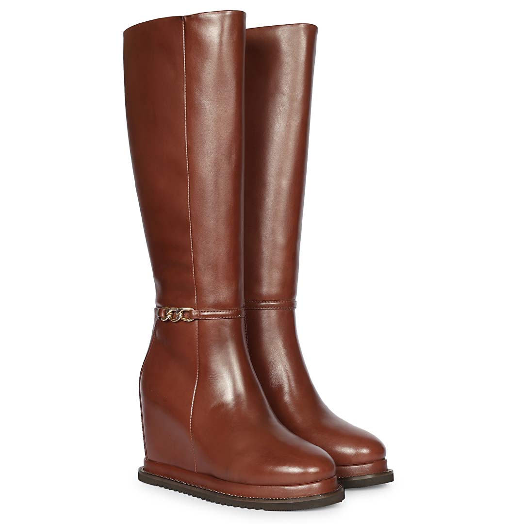 A pair of knee-high brown leather boots with a low wedge heel and a decorative horsebit detail on the side