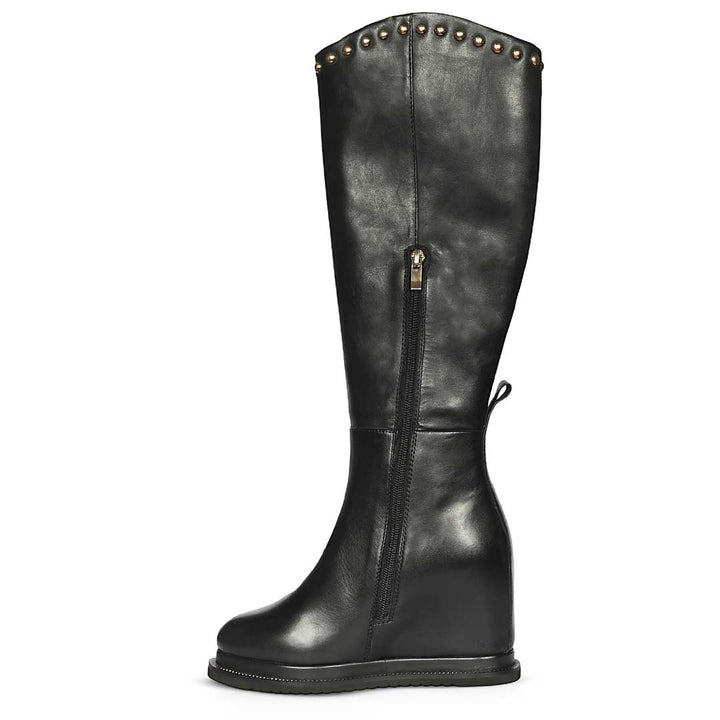 A black leather knee-high boot with a wedge heel, side zipper, and decorative metal studs along the top collar