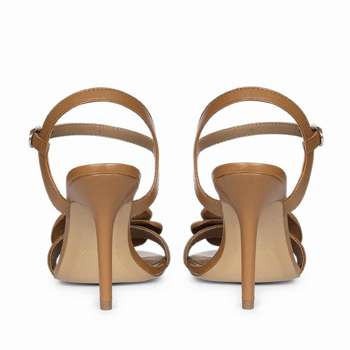 A pair of tan leather high-heeled sandals shown from the back, featuring an ankle strap