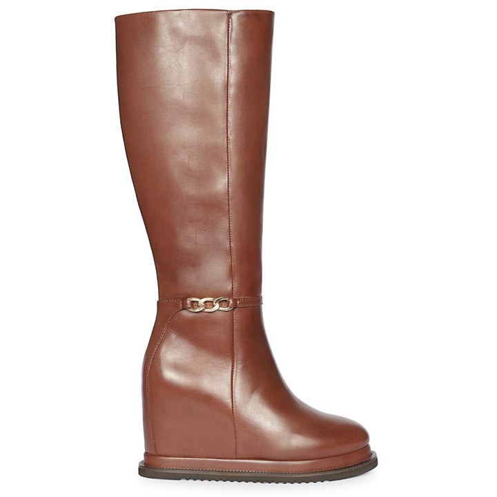A brown leather knee-high riding boot with a wedge heel and a decorative gold-tone chain strap detail