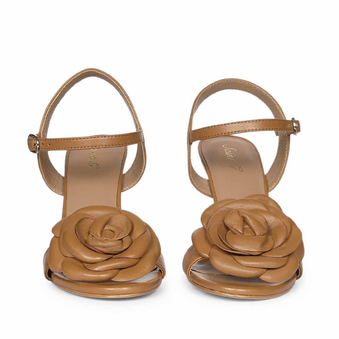 A pair of tan leather high-heeled sandals with a large 3D rose detail on the front and an adjustable ankle strap